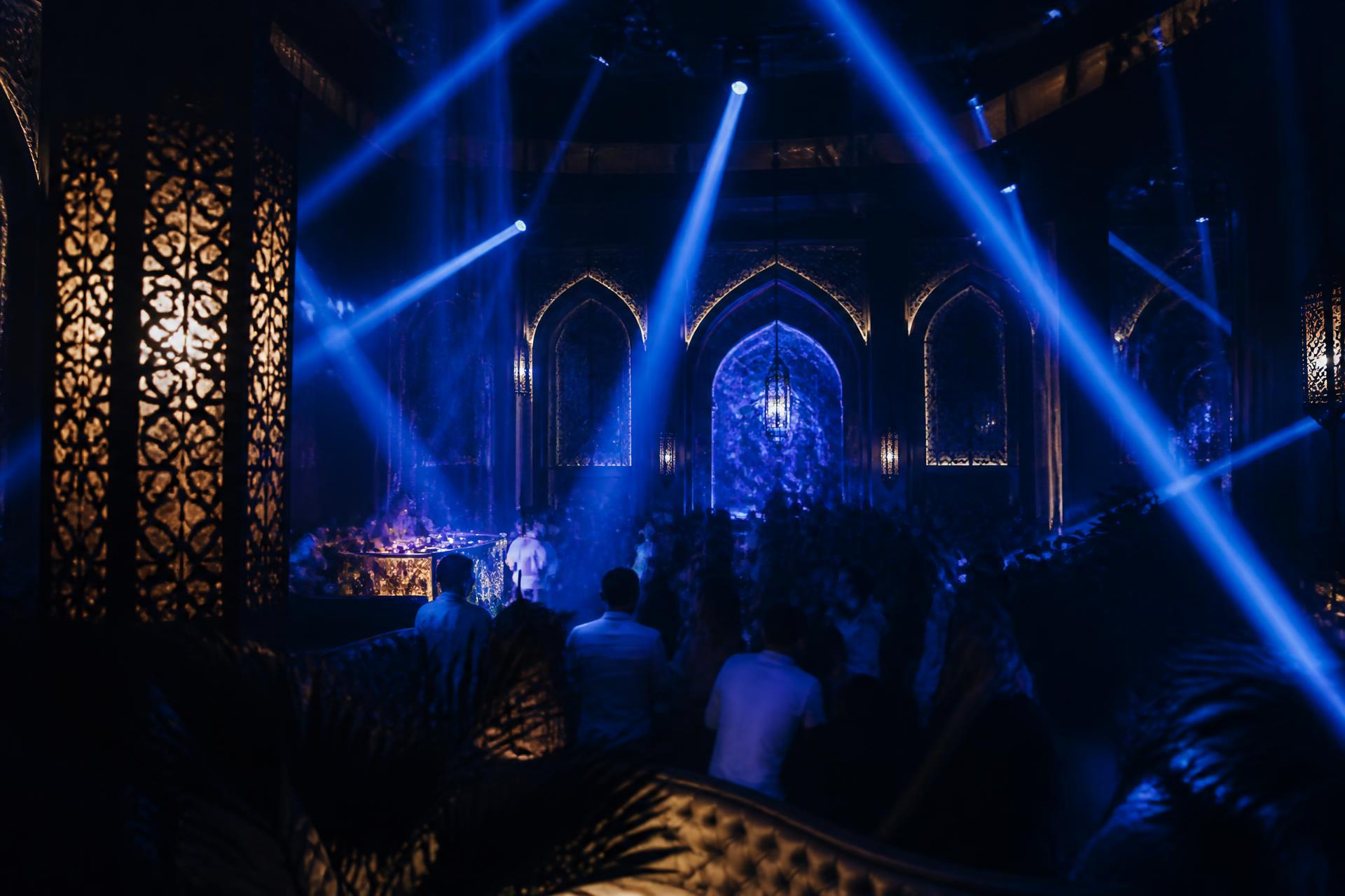 Neon-lit luxury nightclub interior in Marrakech with blue light beams and moorish arches